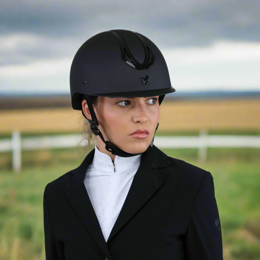 Person wearing a black riding helmet and dark coat on a gray background