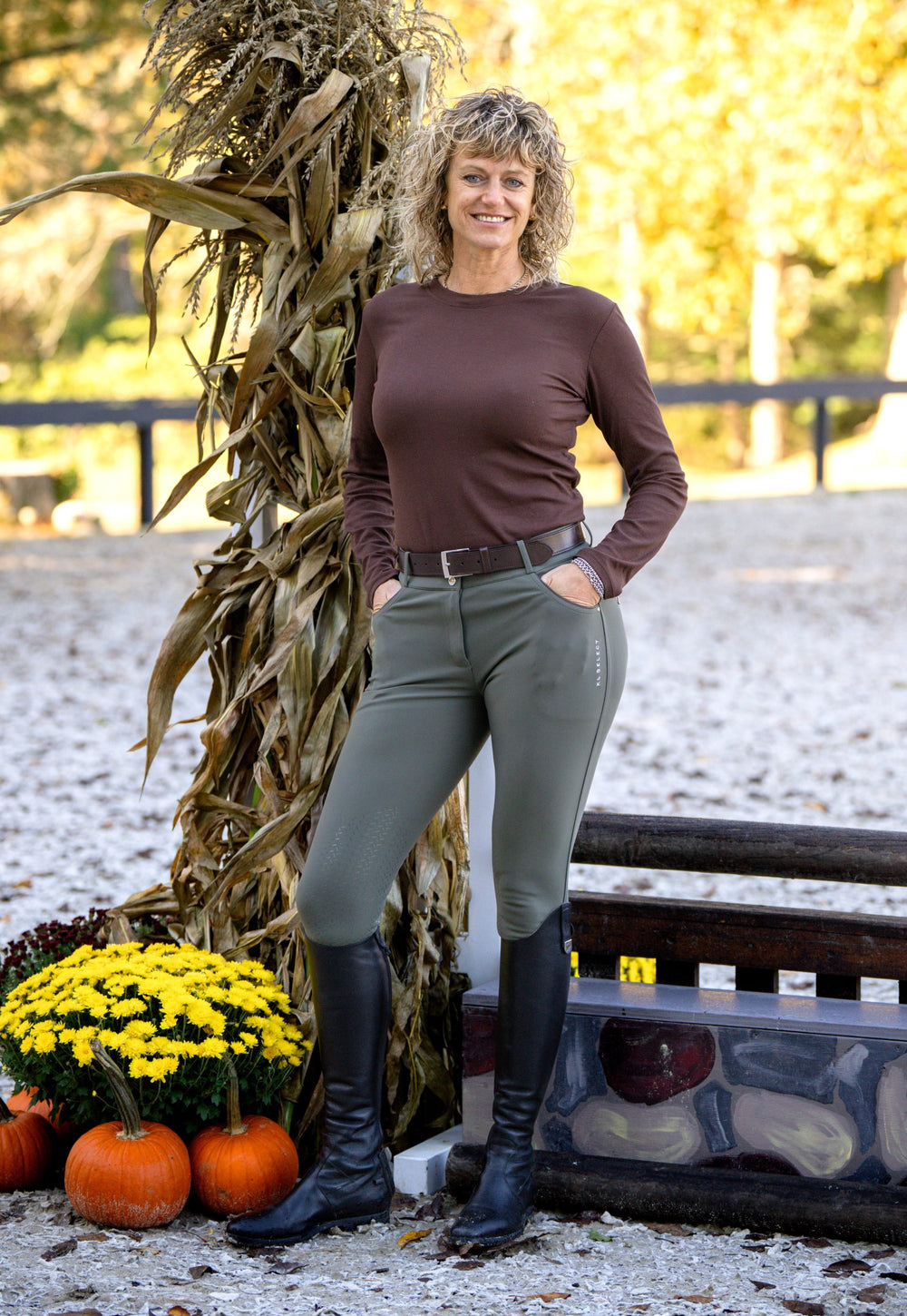 Woman standing next to a corn stalk and pumpkins in a snowy outdoor setting